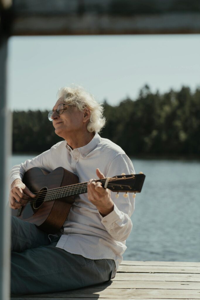 Elderly Guitarist Sitting on Pier and Playing